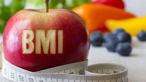 Apfel mit dem eingeritzten Wort „BMI“ und einem Maßband, umgeben von Früchten – Symbol für Gewichtskontrolle und gesunde Ernährung.