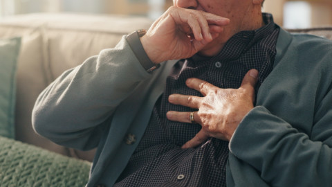 Männliche Person hat eine Infektion und fasst sich jetzt mit Beschwerden ans Herz